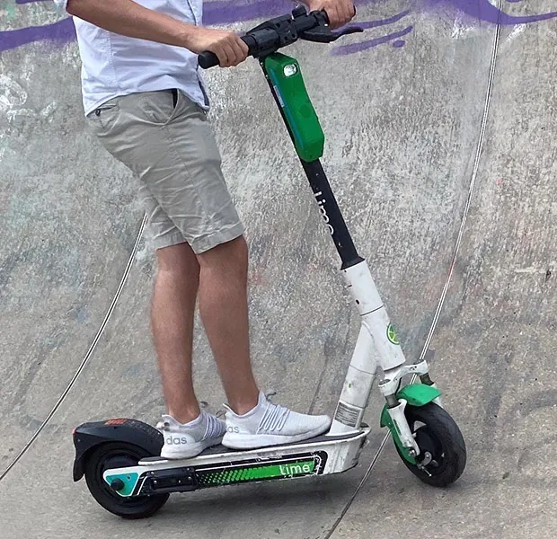 Person steht mit einem Leih-E-Scooter auf einer Skaterampe
