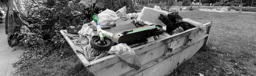 Alter E-Scooter liegt in einem Müllcontainer